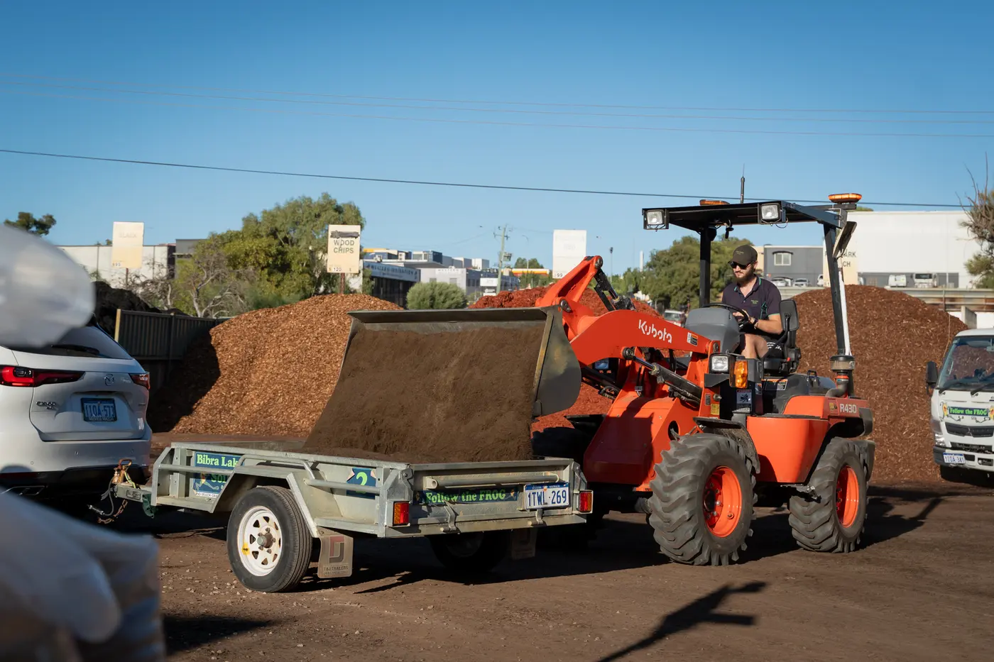 A loader tipping a scoop of mulch into a customer's Bibra Lake box trailer at the yard